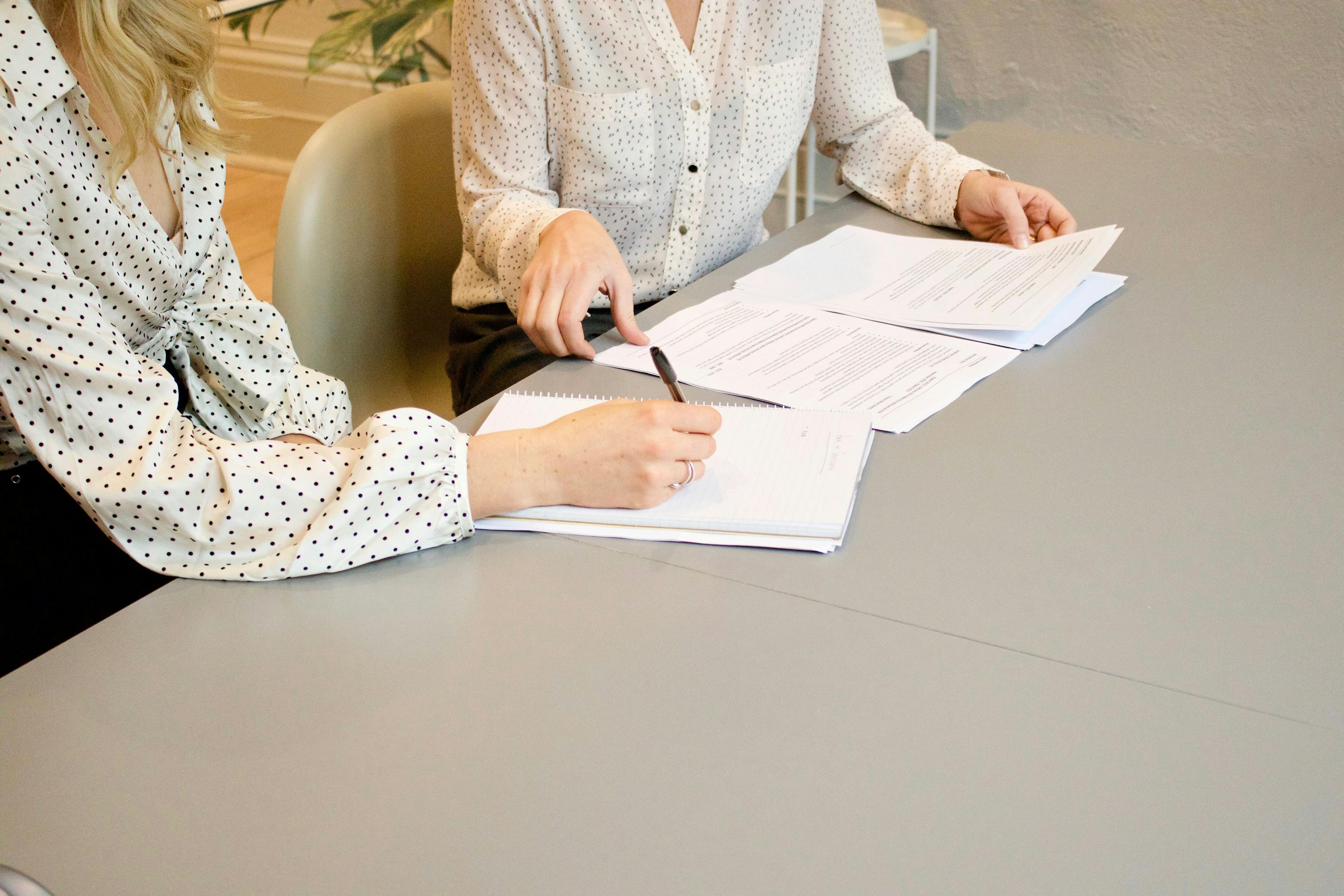 two women sitting around a table signing papers.