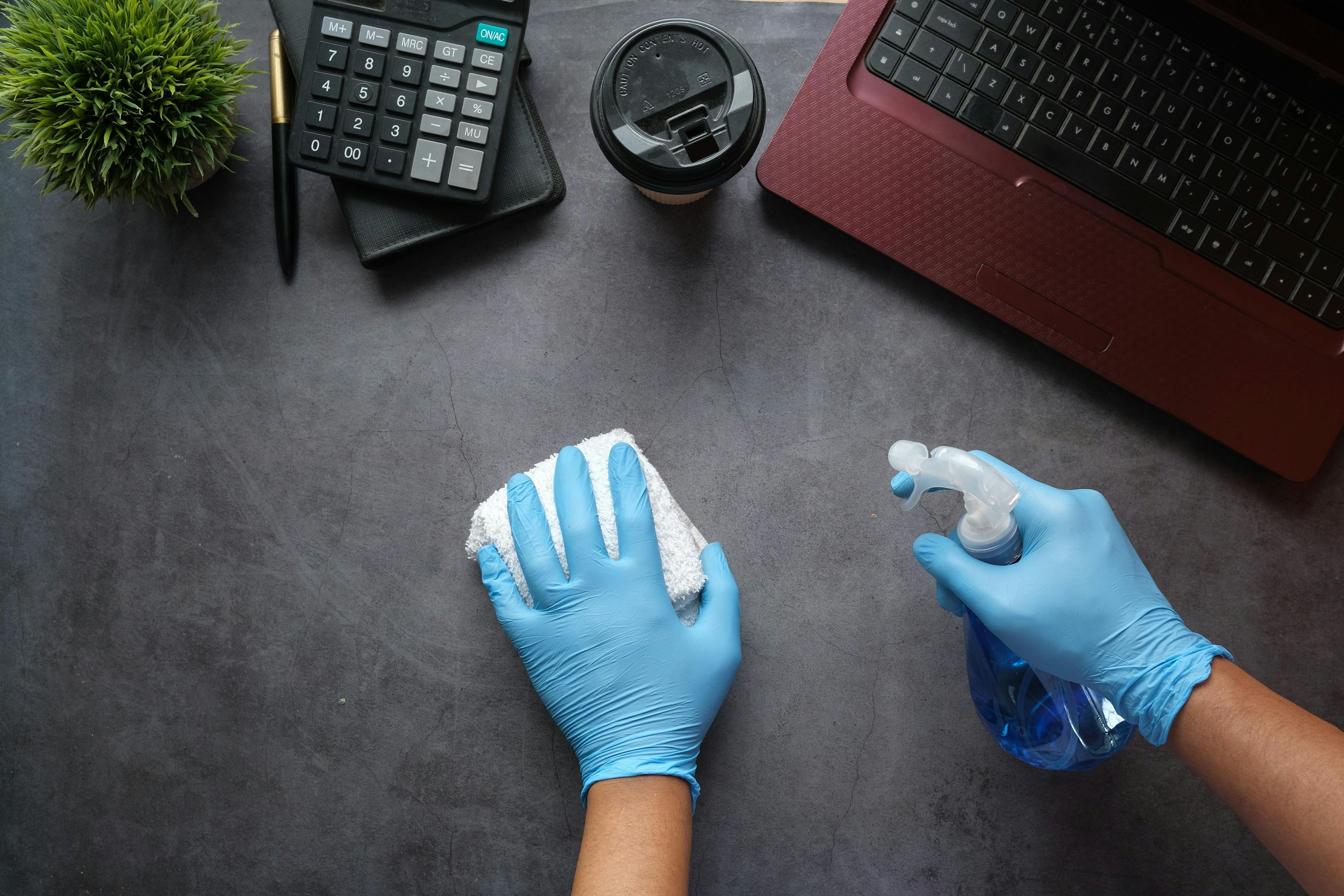 женщина в перчатка протирает рабочее место, ноутбук, кофе, калькулятор, ручка