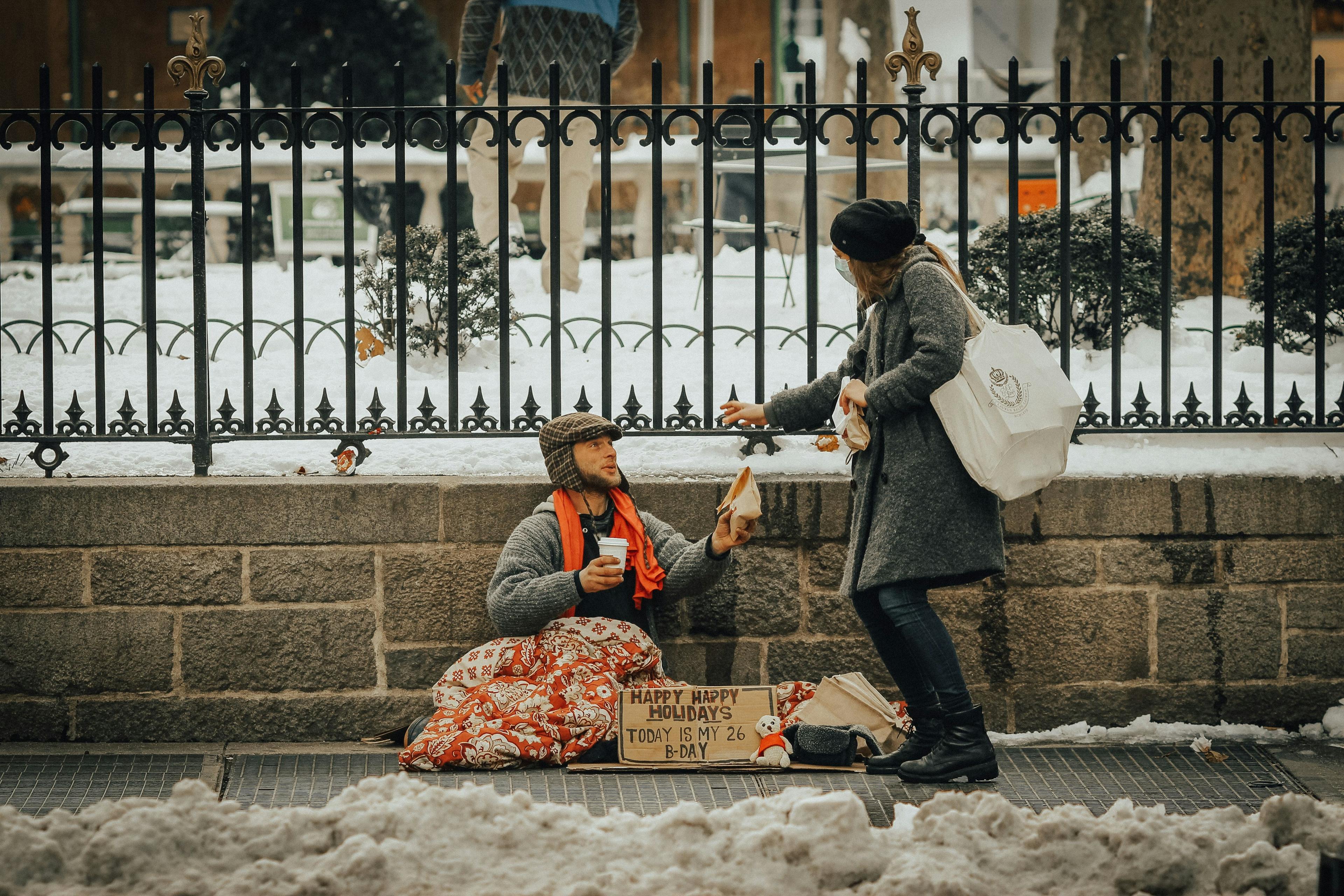 бездомный на улице получает кофе и булочку от прохожей